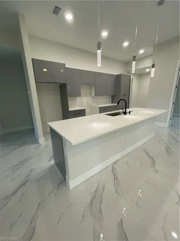 Kitchen with gray cabinetry, pendant lighting, sink, and a kitchen island with sink