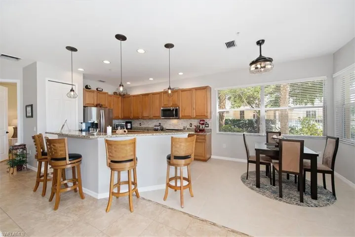 Kitchen with backsplash, a kitchen breakfast bar, hanging light fixtures, stainless steel appliances, and light stone countertops