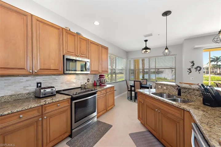 Kitchen with brown cabinetry, stainless steel appliances, light stone countertops, pendant lighting, and recessed lighting