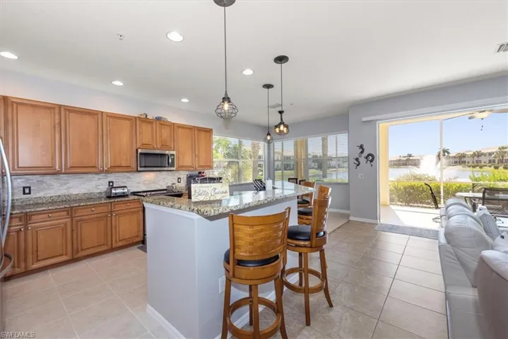 Kitchen featuring a kitchen breakfast bar, brown cabinetry, light stone counters, decorative backsplash, and hanging light fixtures