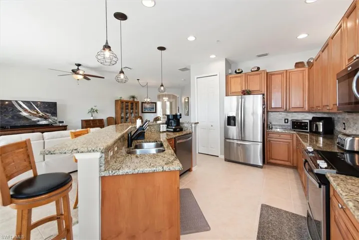 Kitchen featuring pendant lighting, a kitchen breakfast bar, stainless steel appliances, light stone counters, and an island with sink