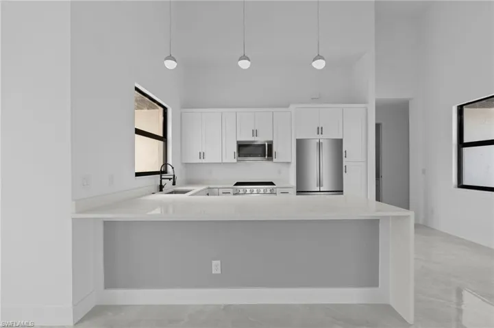 Kitchen with white cabinetry, appliances with stainless steel finishes, sink, and pendant lighting