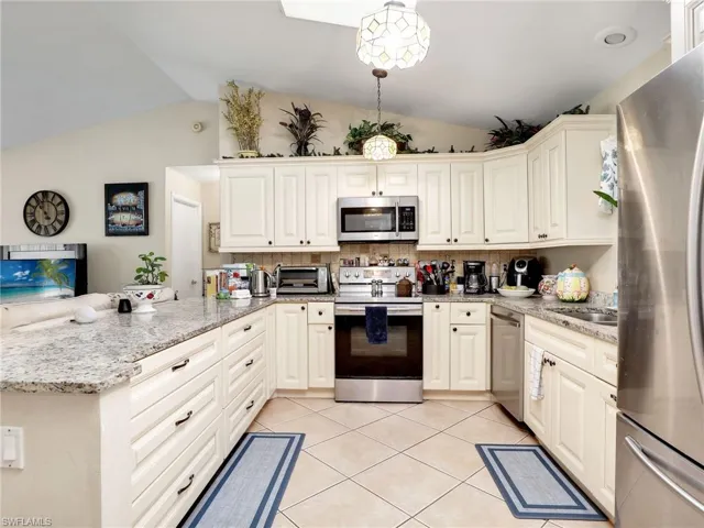 Kitchen featuring decorative light fixtures, kitchen peninsula, vaulted ceiling, and stainless steel appliances