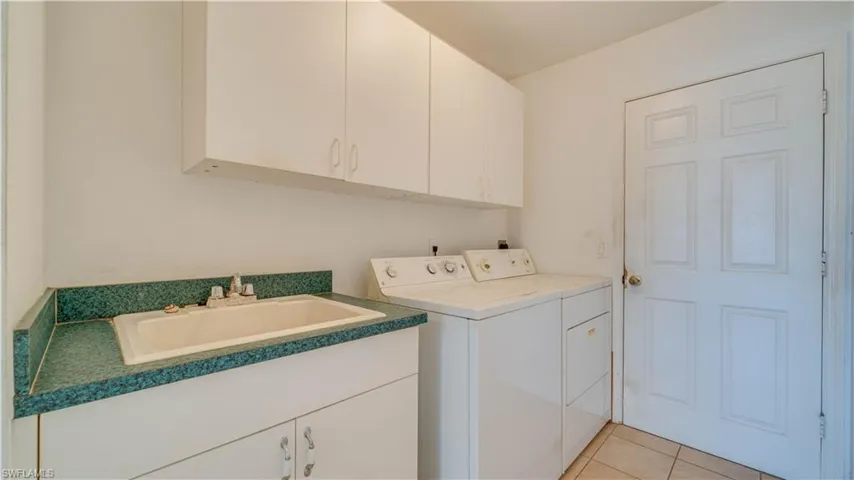 Laundry area with washing machine and dryer, cabinet space, a sink, and light tile patterned floors