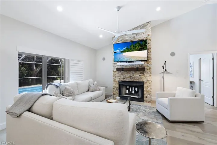Living room with a stone fireplace, ceiling fan, light hardwood / wood-style floors, and high vaulted ceiling