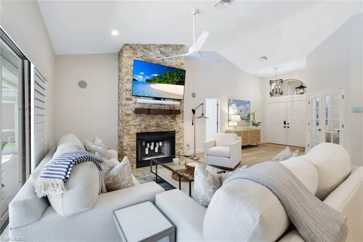 Living room featuring french doors, light hardwood / wood-style flooring, ceiling fan, a fireplace, and high vaulted ceiling