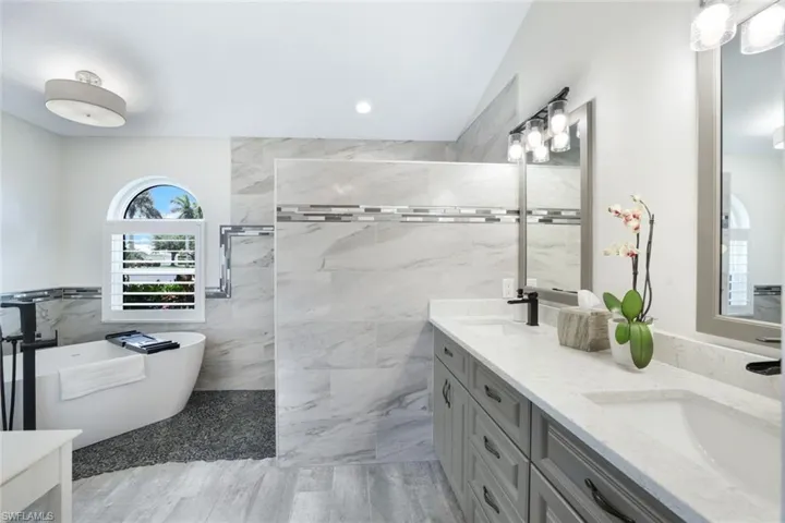 Bathroom with double vanity, tile walls, tile patterned floors, and a tub