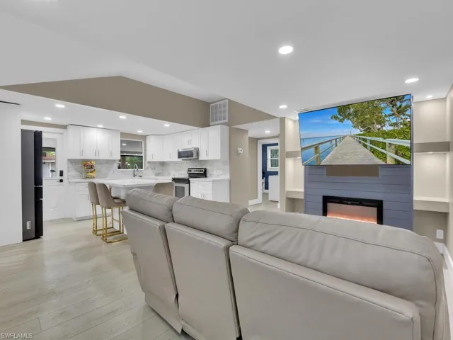 Living room with recessed lighting, a glass covered fireplace, light wood-style floors, and lofted ceiling