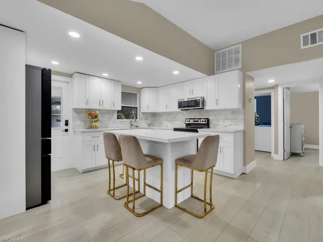 Kitchen with white cabinetry, a kitchen bar, refrigerator, recessed lighting, and black electric range oven
