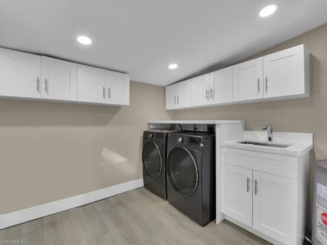 Laundry area with light wood-type flooring, washer and clothes dryer, cabinet space, recessed lighting, and water heater