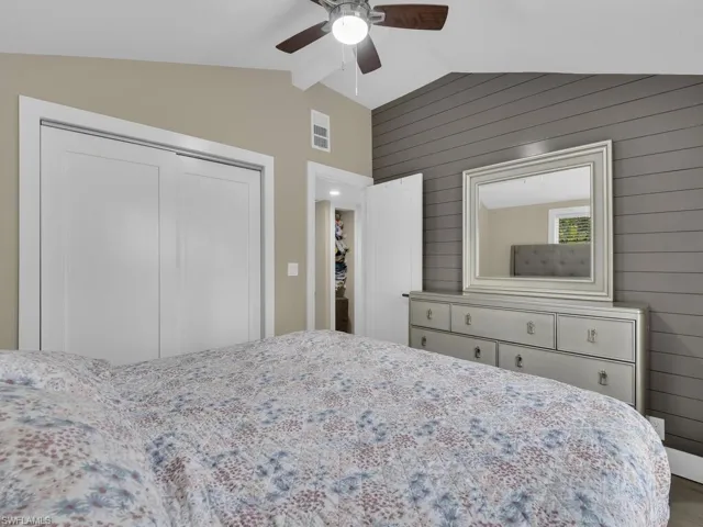 Bedroom featuring vaulted ceiling, wood walls, a closet, and ceiling fan