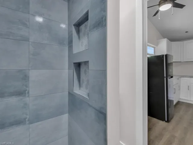 Bathroom view of freestanding refrigerator, wood finished floors, tiled shower, and a ceiling fan