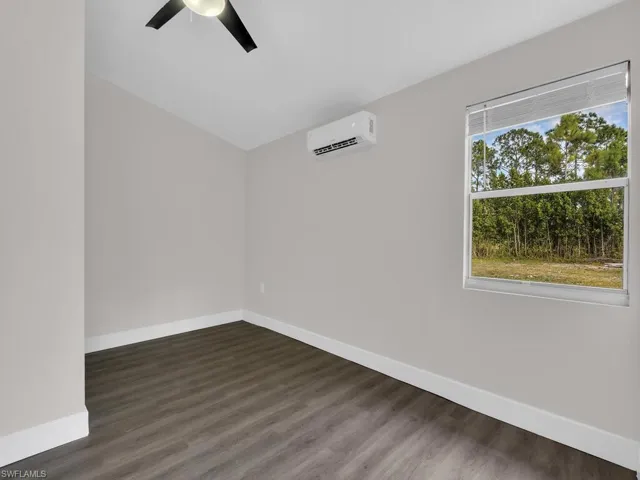 Unfurnished room featuring dark wood-style floors, a wall unit AC, and a ceiling fan