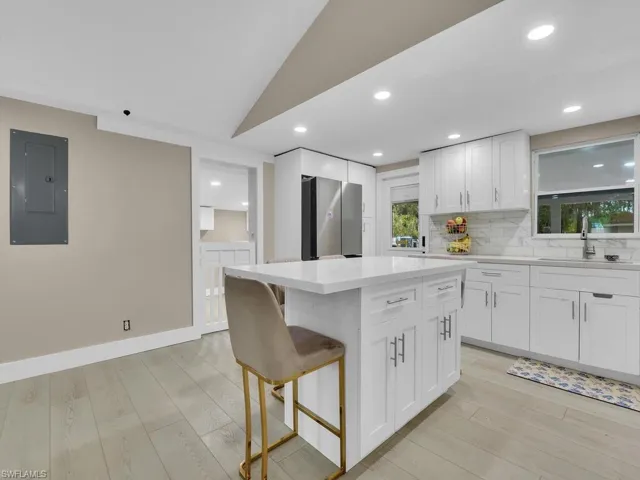 Kitchen featuring white cabinetry, electric panel, light wood-style flooring, tasteful backsplash, and freestanding refrigerator