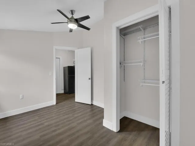 Unfurnished bedroom with freestanding refrigerator, dark wood finished floors, a closet, and a ceiling fan