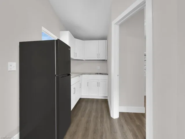 Kitchen featuring freestanding refrigerator, white cabinets, light countertops, and dark wood-style flooring
