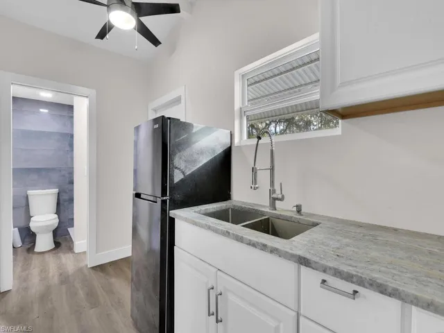 Kitchen with light stone counters, white cabinetry, freestanding refrigerator, light wood-style flooring, and ceiling fan