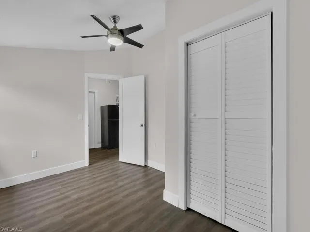Unfurnished bedroom featuring a closet, freestanding refrigerator, dark wood-style flooring, and ceiling fan