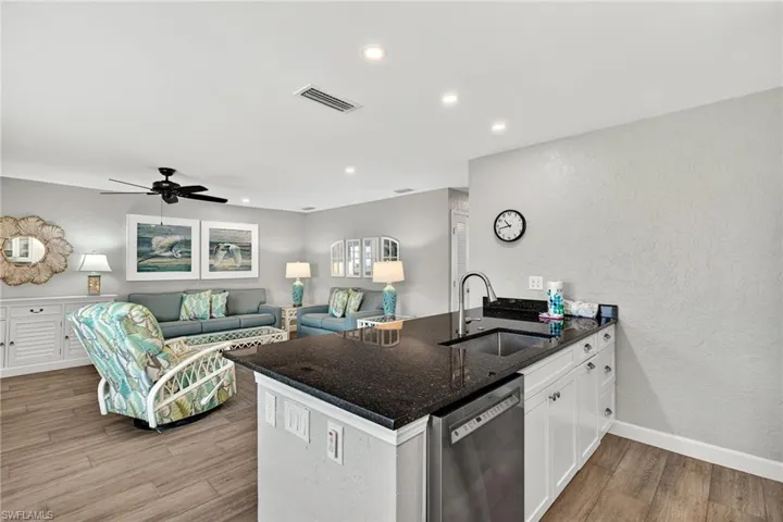 Kitchen with a peninsula, a textured wall, dark stone countertops, dishwasher, and white cabinetry
