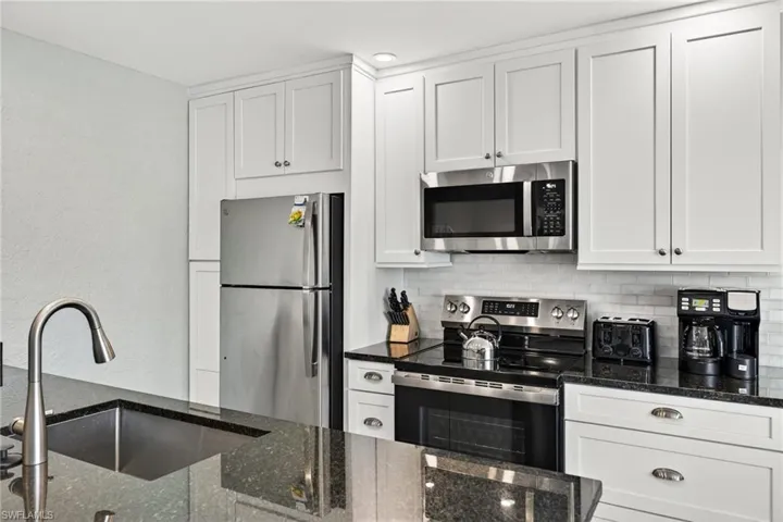 Kitchen with stainless steel appliances, dark stone counters, white cabinets, backsplash, and a textured wall