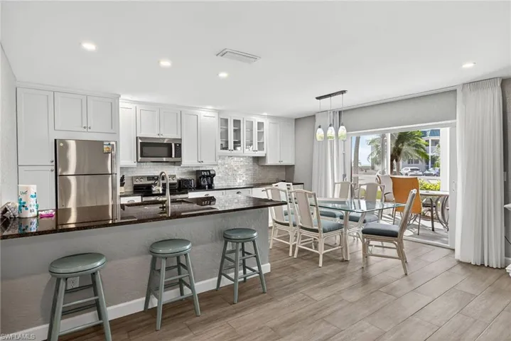 Kitchen with glass insert cabinets, a breakfast bar, appliances with stainless steel finishes, white cabinets, and dark stone counters