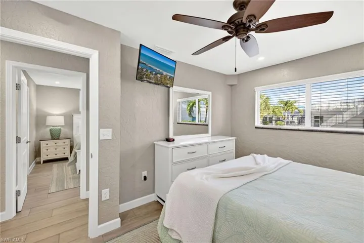 Bedroom with a textured wall, light wood finished floors, and ceiling fan