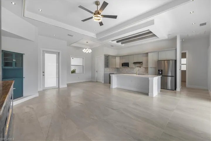 Unfurnished living room featuring ceiling fan, a raised ceiling, recessed lighting, and a chandelier