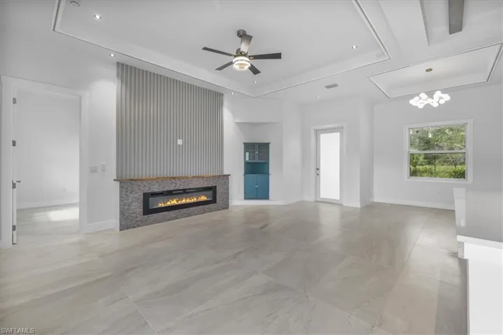 Unfurnished living room featuring a raised ceiling, a glass covered fireplace, a ceiling fan, recessed lighting, and a chandelier