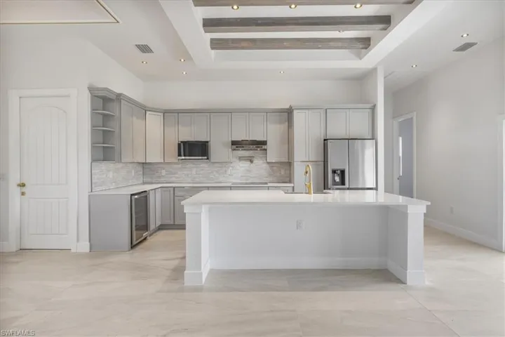 Kitchen with stainless steel refrigerator with ice dispenser, gray cabinets, beverage cooler, open shelves, and decorative backsplash