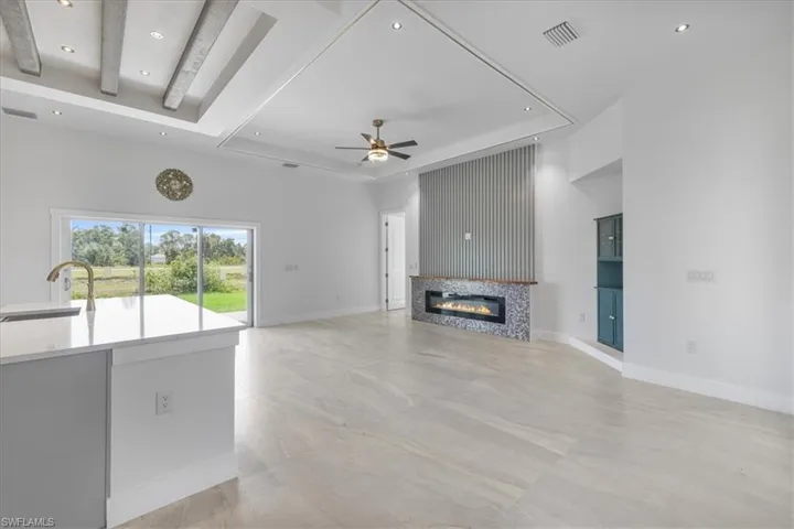 Unfurnished living room featuring ceiling fan, a fireplace, recessed lighting, and beam ceiling
