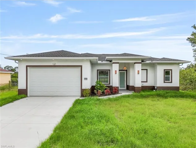 Prairie-style home featuring a garage, driveway, stucco siding, a front lawn, and roof with shingles
