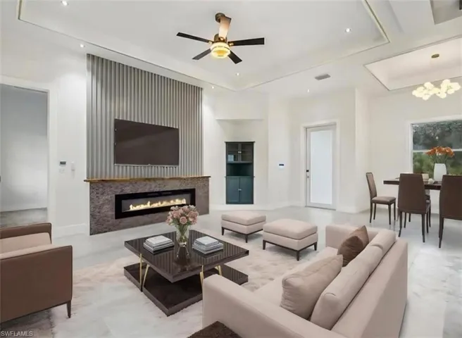 Living area with a raised ceiling, a glass covered fireplace, built in shelves, a chandelier, and recessed lighting