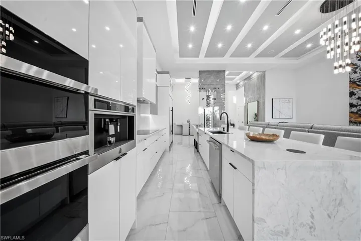Kitchen featuring modern cabinets, white cabinetry, stainless steel appliances, light stone counters, and island
