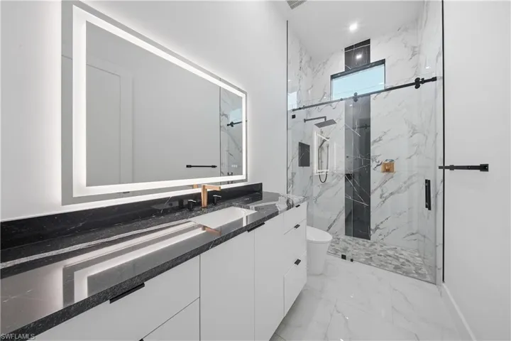 Full bath featuring vanity, a marble finish shower, light marble finish floors, and recessed lighting