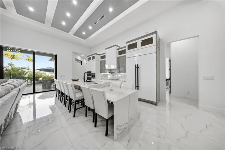 Kitchen with glass fronted cabinets, white cabinetry, a spacious island, light stone counters, and a kitchen bar