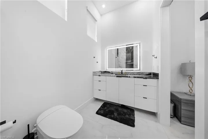 Full bathroom featuring vanity, light marble finish flooring, a high ceiling, and a shower