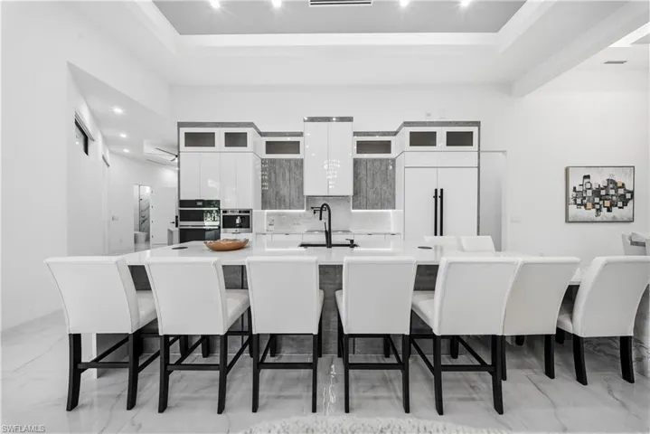 Kitchen featuring white cabinets, a kitchen breakfast bar, glass insert cabinets, a high ceiling, and recessed lighting