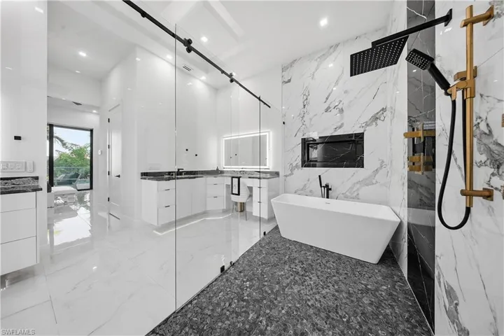 Full master bathroom with vanity, a marble finish shower, a soaking tub, light marble finish flooring, and stone wall