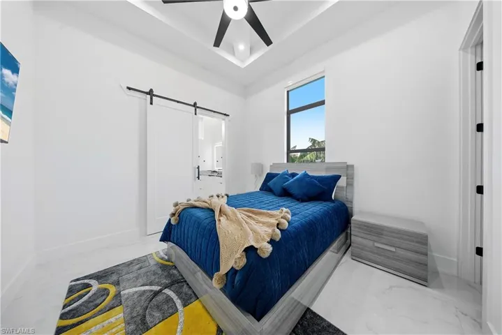 Bedroom with a barn door, ensuite bathroom,  a ceiling fan, and a tray & coffered ceiling