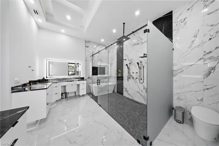 Master Bathroom with vanity, recessed lighting, a marble finish shower, tray ceilings