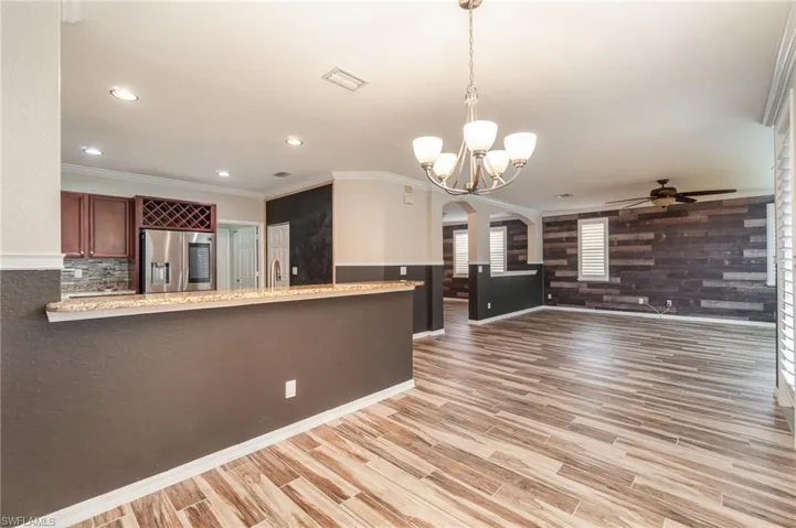 Overlooking Kitchen with light hardwood / wood-style flooring, kitchen peninsula, ceiling fan with notable chandelier, stainless steel refrigerator with ice dispenser, and ornamental molding