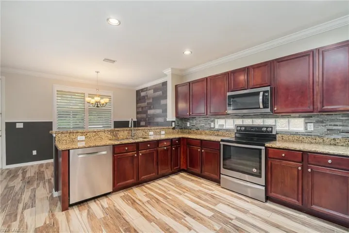 Kitchen featuring light wood-type flooring, sink, light stone counters, appliances with stainless steel finishes, and kitchen peninsula