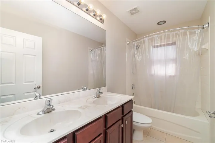 Full bathroom with shower / bath combo with shower curtain, tile patterned floors, toilet, and dual bowl vanity
