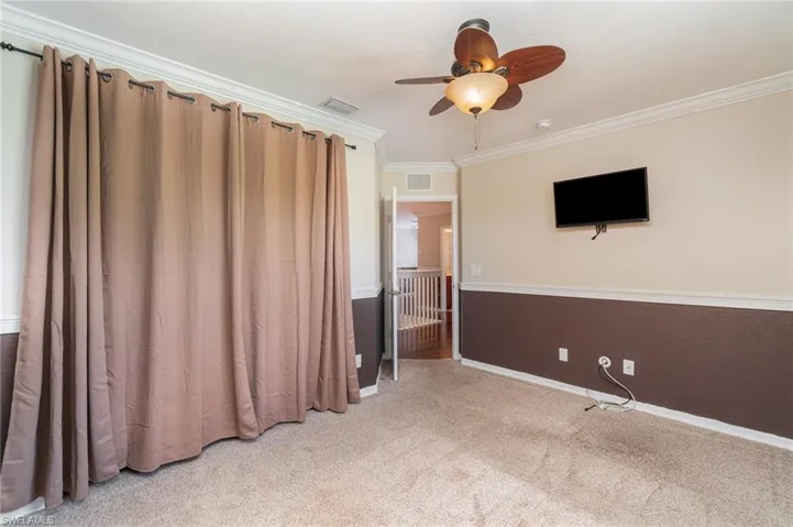 Empty room with ornamental molding, light colored carpet, and ceiling fan