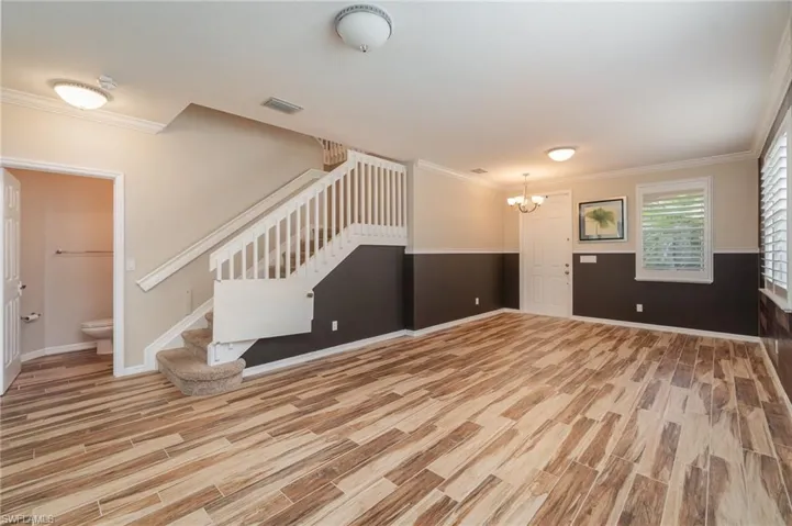 Unfurnished living room featuring an inviting chandelier, crown molding, and light hardwood / wood-style flooring