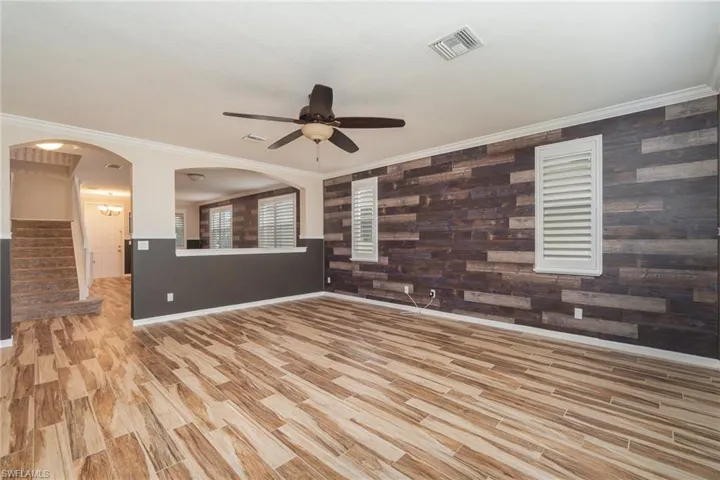 Unfurnished living room featuring wood walls, ceiling fan, crown molding, and light hardwood / wood-style floors