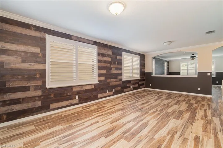 Unfurnished living room featuring crown molding, wood walls, light hardwood / wood-style flooring, and ceiling fan