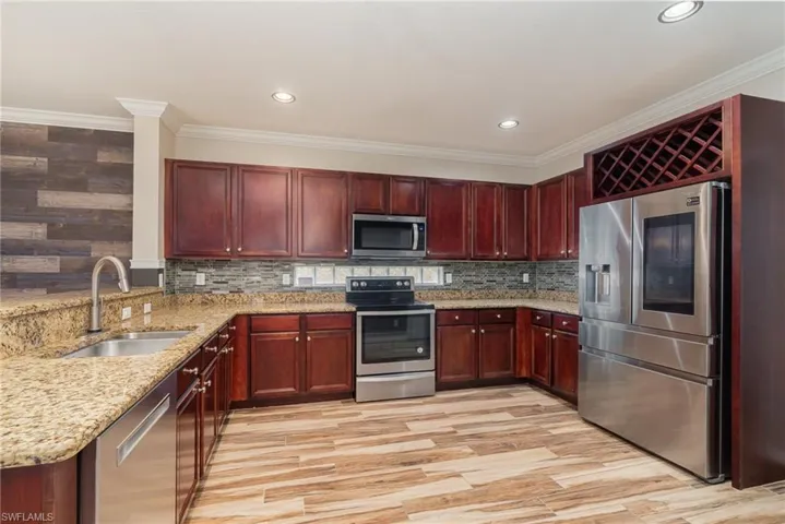 Kitchen with sink, light stone countertops, appliances with stainless steel finishes, light hardwood / wood-style flooring, and backsplash