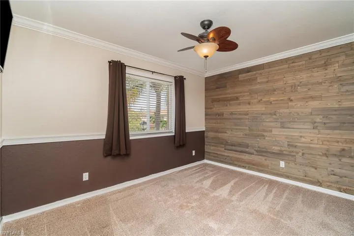 Empty room featuring ceiling fan, wood walls, crown molding, and carpet flooring