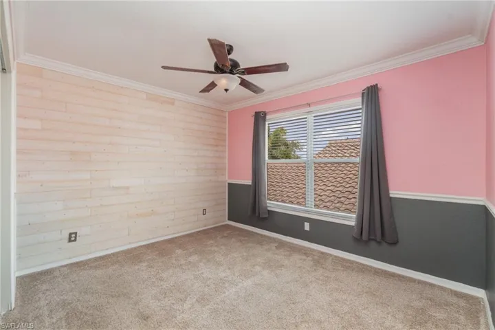 Carpeted spare room with ornamental molding, wooden walls, and ceiling fan